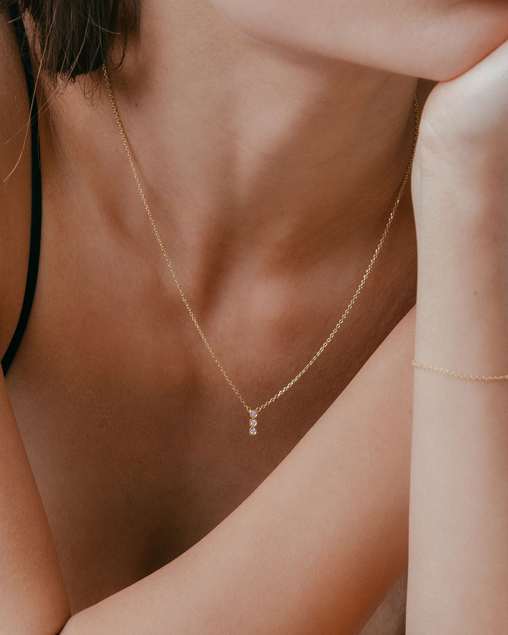mulher de blusa de alcinha preta usando colar minimalista feito à mão em ouro 18k com três diamantes pequenos do mesmo tamanho enfileirados verticalmente