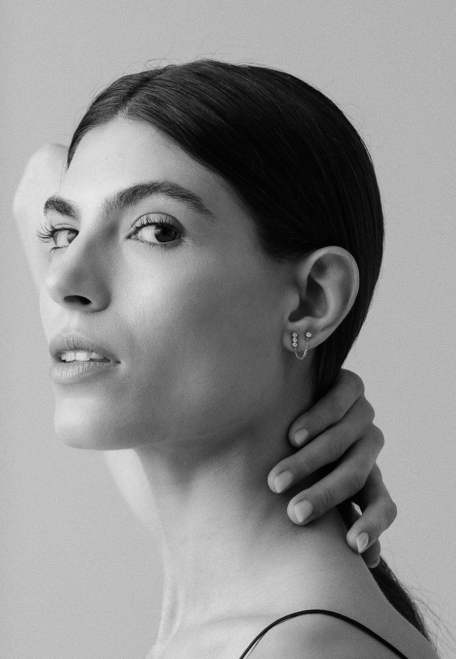 foto em preto e branco de mulher usando brincos minimalistas feitos à mão em ouro 18k com diamantes e extensor de corrente que liga os dois brincos