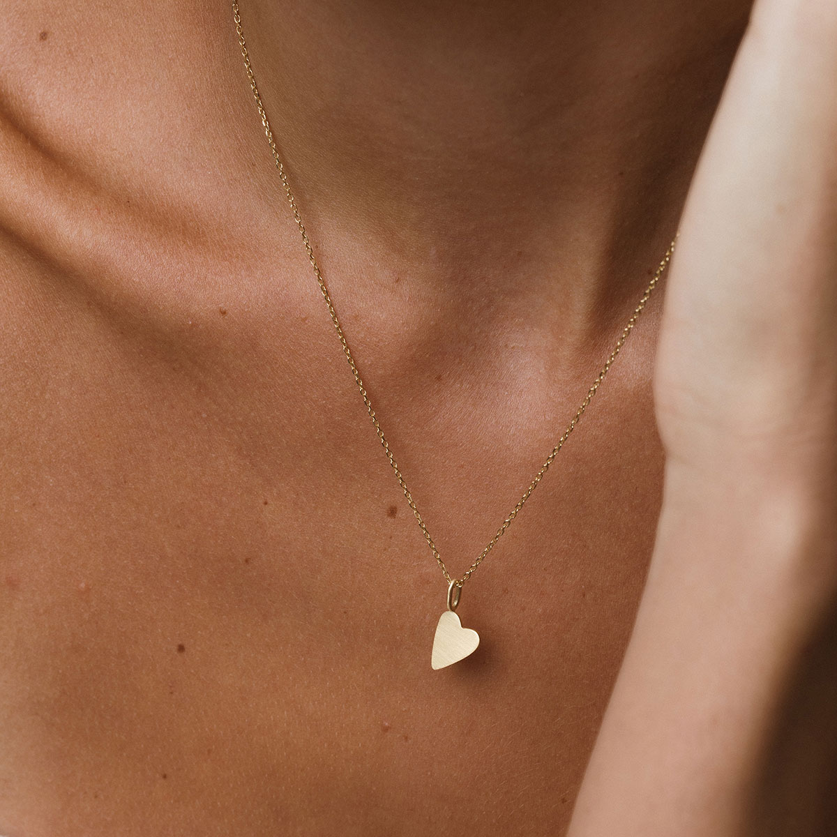 foto com foco no colo de uma mulher usando um colar e um pingente de coração com acabamento fosco em ouro 18k