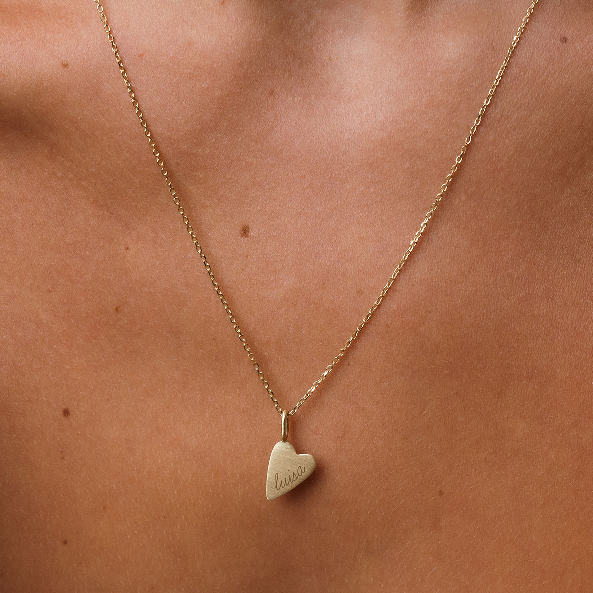 mulher usando um colar com pingente de coração com gravação personalizada de nome em ouro 18k