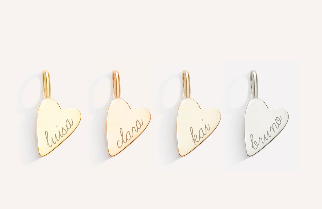 foto de quatro pingentes de coração, nas ordem de tonalidades amarelo, rosé, champagne e branco, com gravação dos nomes "luisa", "clara", "kai" e "bruno" respectivamente, em letra cursiva e com acabamento fosco, em ouro 18k, sobre fundo branco