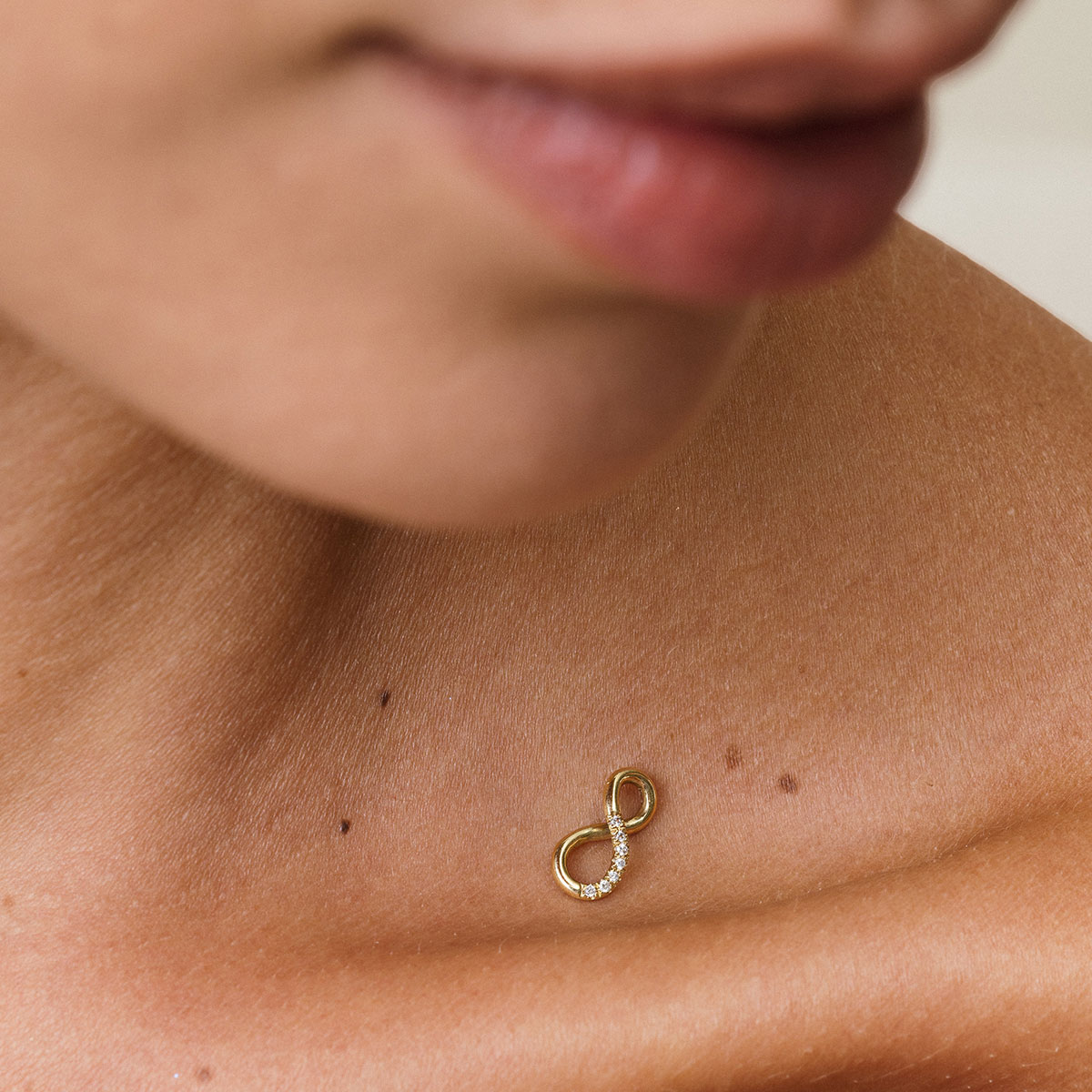mulher com pingente infinito em ouro amarelo e diamantes sobre a pele