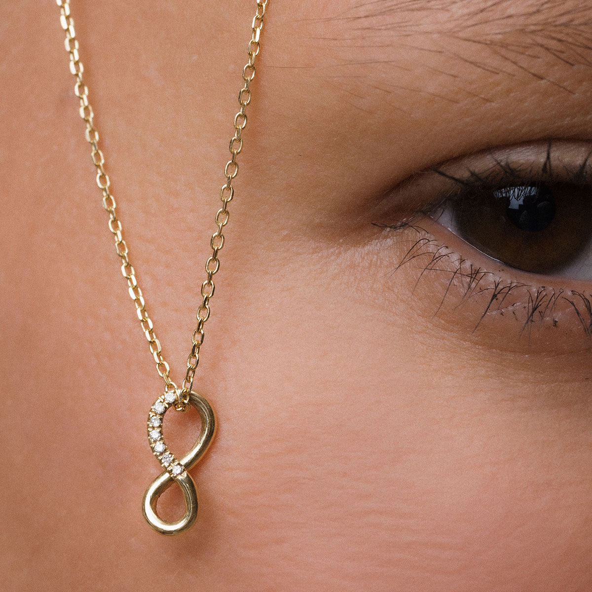 mulher com corrente com pingente infinito em ouro amarelo e diamantes pendurado próximo ao olho castanho