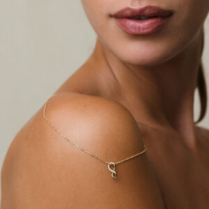 corrente com pingente infinito em ouro amarelo e diamantes sobre ombro de mulher