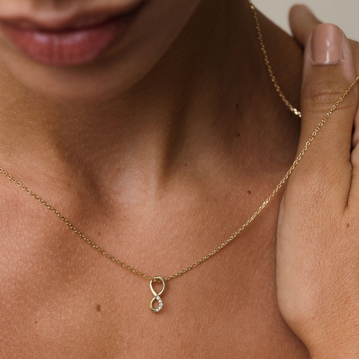 mulher olhando para baixo, vestindo corrente com pingente infinito em ouro amarelo