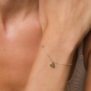foto com foco no pulso de uma mulher usando uma pulseira de ouro 18k com um pingente de coração