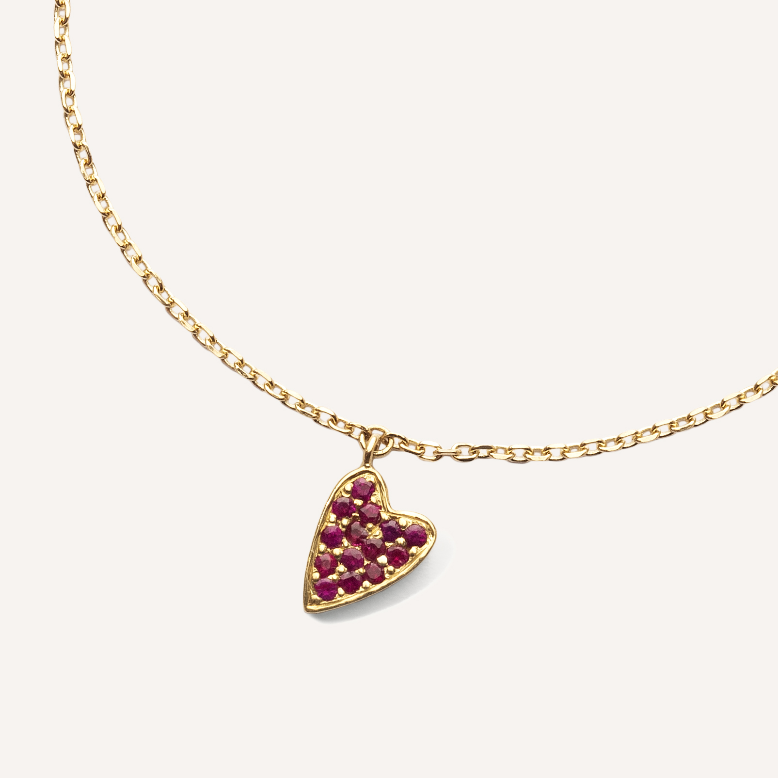 pulseira de ouro amarelo 18k com um pingente de coração cravejado com 14 rubis sobre fundo branco