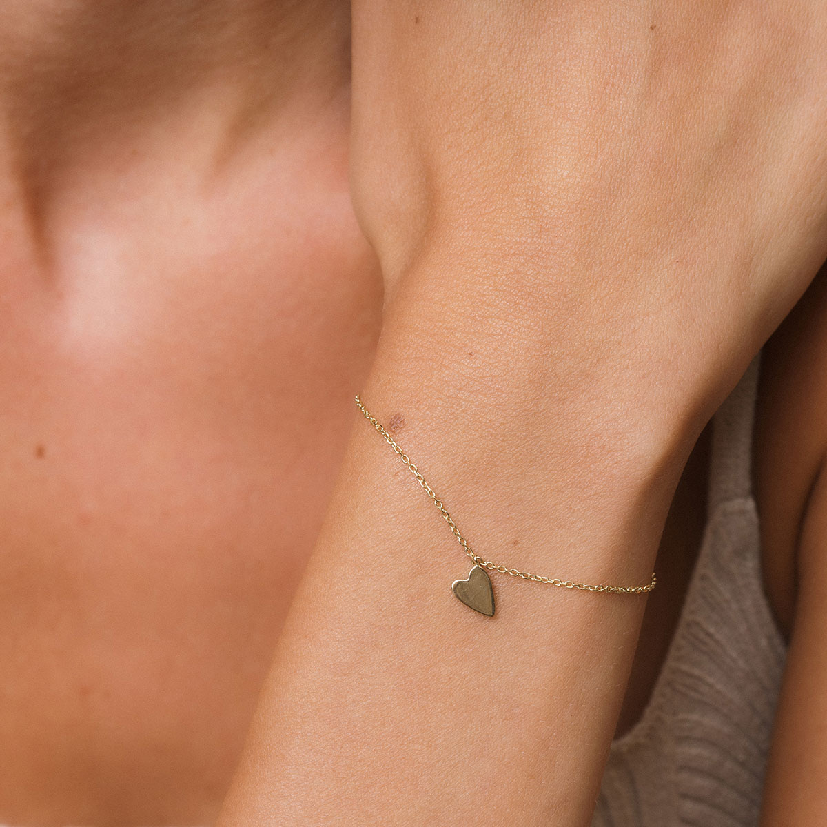 foto com foco no pulso de uma mulher usando uma pulseira de ouro 18k com um pingente de coração