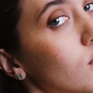 Imagem de close evidenciando o Brinco Esmeralda com Diamantes Baguete da Joias Liê. A peça apresenta uma esmeralda de 1,28 ct em lapidação retangular, ladeada por dois diamantes em corte baguete. Um design elegante, simétrico e sofisticado, que combina o verde vibrante da esmeralda com o brilho limpo e moderno dos diamantes.