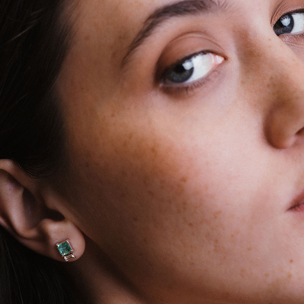 Imagem de close evidenciando o Brinco Esmeralda com Diamantes Baguete da Joias Liê. A peça apresenta uma esmeralda de 1,28 ct em lapidação retangular, ladeada por dois diamantes em corte baguete. Um design elegante, simétrico e sofisticado, que combina o verde vibrante da esmeralda com o brilho limpo e moderno dos diamantes.