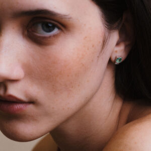Imagem de close evidenciando o Brinco Esmeralda com Diamantes Baguete da Joias Liê. A peça apresenta uma esmeralda de 1,28 ct em lapidação retangular, ladeada por dois diamantes em corte baguete. Um design elegante, simétrico e sofisticado, que combina o verde vibrante da esmeralda com o brilho limpo e moderno dos diamantes.