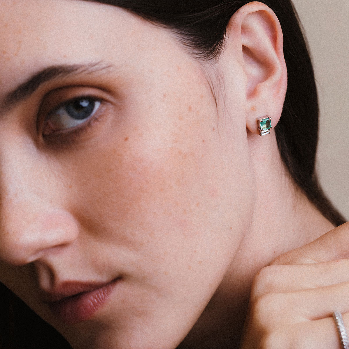 Imagem de close evidenciando o Brinco Esmeralda com Diamantes Baguete da Joias Liê. A peça apresenta uma esmeralda de 1,28 ct em lapidação retangular, ladeada por dois diamantes em corte baguete. Um design elegante, simétrico e sofisticado, que combina o verde vibrante da esmeralda com o brilho limpo e moderno dos diamantes.