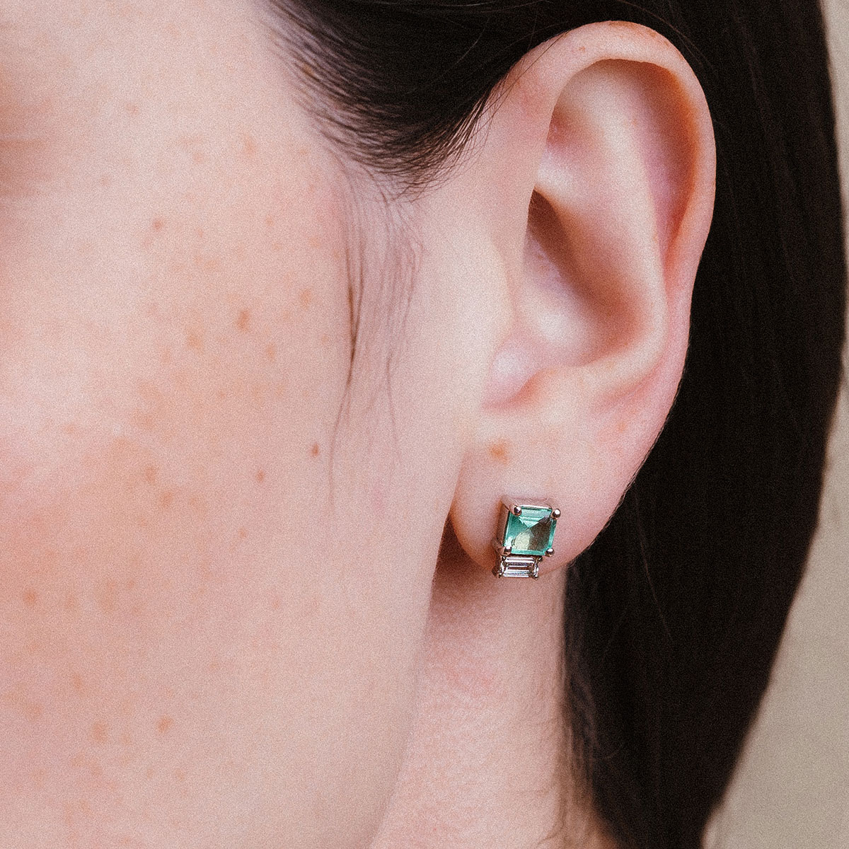 Imagem de close evidenciando o Brinco Esmeralda com Diamantes Baguete da Joias Liê. A peça apresenta uma esmeralda de 1,28 ct em lapidação retangular, ladeada por dois diamantes em corte baguete. Um design elegante, simétrico e sofisticado, que combina o verde vibrante da esmeralda com o brilho limpo e moderno dos diamantes.