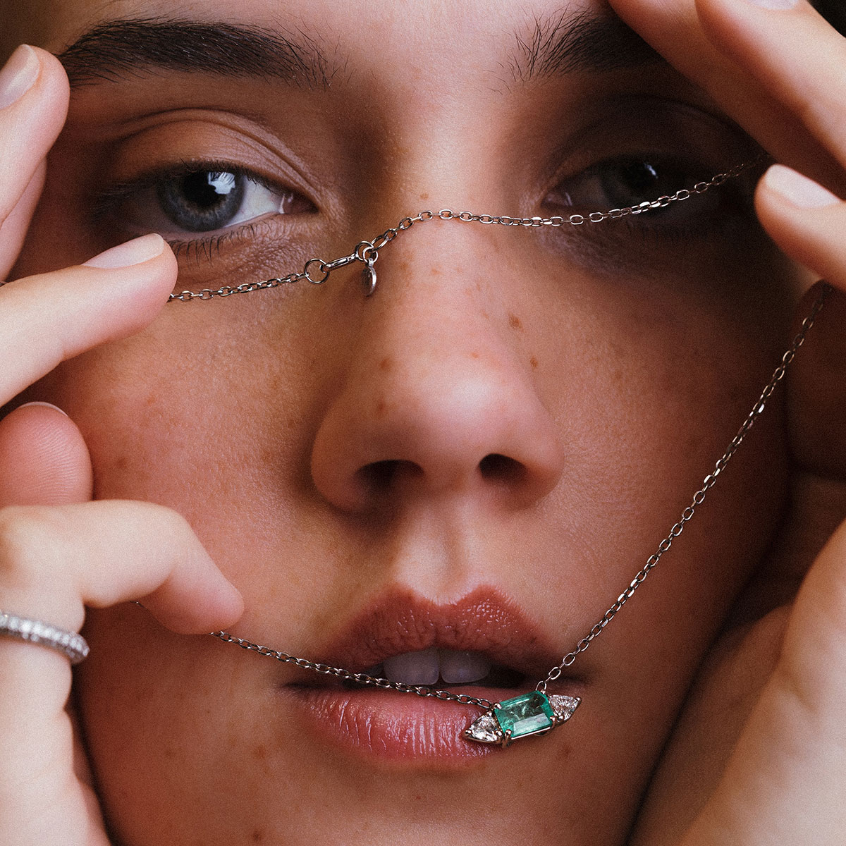 Close no rosto de mulher com colar em destaque, mostrando esmeralda central e diamantes trillion em corrente de ouro branco.