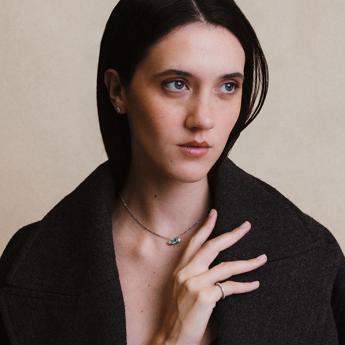 Mulher vestindo casaco preto e usando um colar com esmeralda e dois diamantes trillion da cada lado e corrente delicada em ouro branco 18k, modelo Colar com Esmeralda e Diamantes Trillion - 1,48 ct da Joias Liê