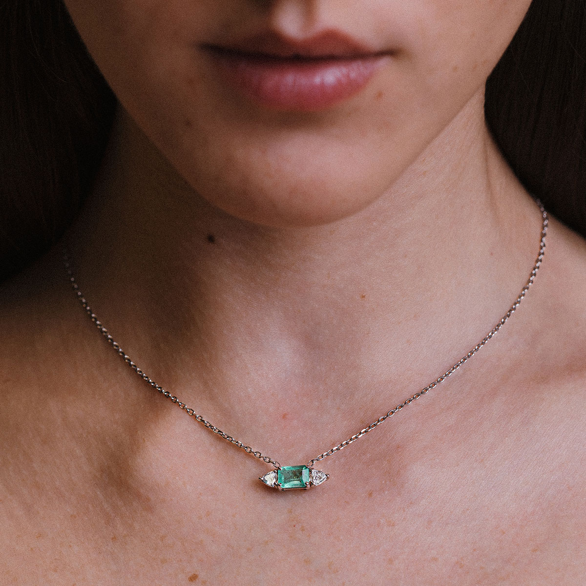 Mulher usando um colar com esmeralda e dois diamantes trillion da cada lado e corrente delicada em ouro branco 18k, modelo Colar com Esmeralda e Diamantes Trillion - 1,48 ct da Joias Liê
