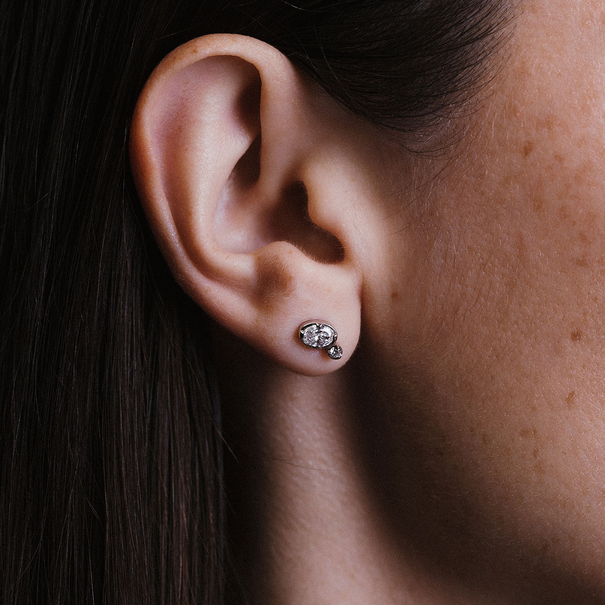 Mulher usando brinco em ouro 18k com diamantes oval e redondo, modelo Cecile da Joias Liê.