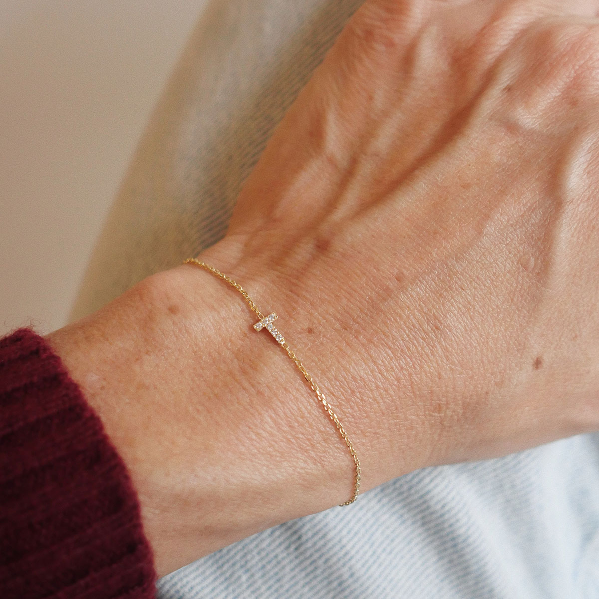 Pulso de mulher vestindo uma pulseira com a letra T, cravejada de diamantes lab grown, e corrente delicada em ouro 18k, modelo Pulseira Inicial com Diamantes da Joias Liê