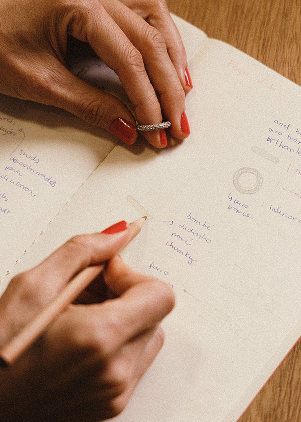 imagem de uma designer de joias fazendo anotações em seu caderno sobre a criação de uma anel em ouro 18k branco e diamantes