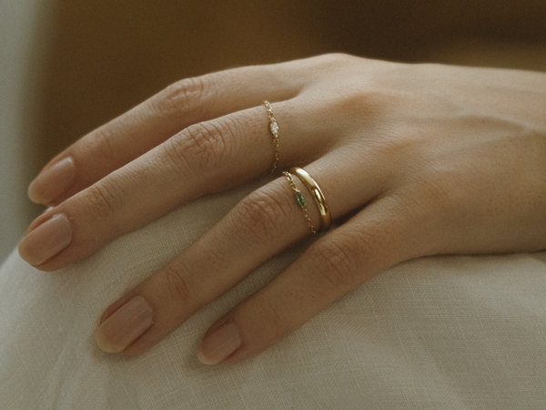 Mão feminina usando os anéis Rastro Diamante Navete e Rastro Esmeralda da Liê Joias, peças minimalistas em ouro 18k com pedras.