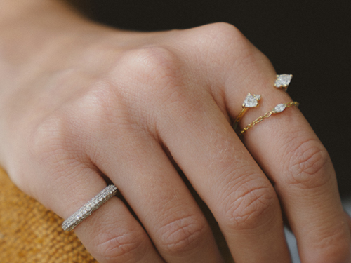 Close das mãos de Iasmine Souza usando o Anel Pinky Ring Diamantes Bombe, o Anel com Diamantes Trillion e o Anel Rastro Diamante Navete da Liê, em registro para a série Em Camadas.