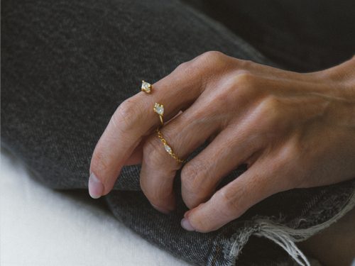 Detalhe da mão de Rachel Bello usando o Anel com Diamantes Trillion e o Anel Rastro Diamante Navete Liê, em registro para a série Em Camadas sobre propósito e autenticidade.