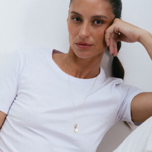 Corrente comprida em ouro 18k com elos longos e pingentes vestidos em modelo de camiseta branca.