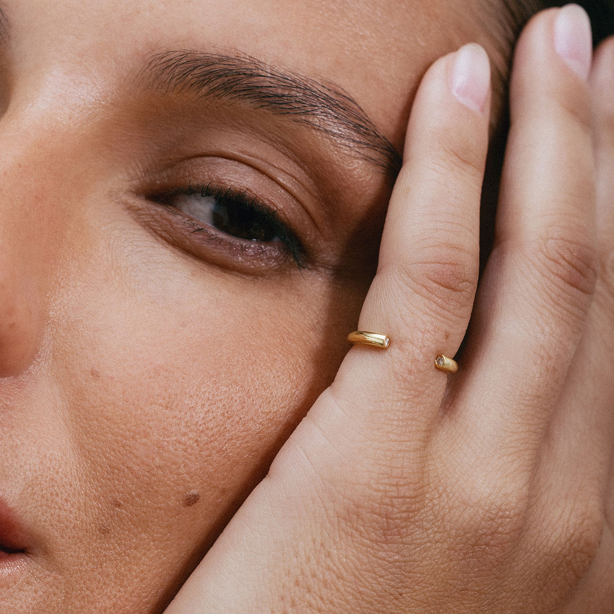 Anel minimalista aberto em ouro 18k com dois diamantes usado no dedo mindinho de uma mão feminina.