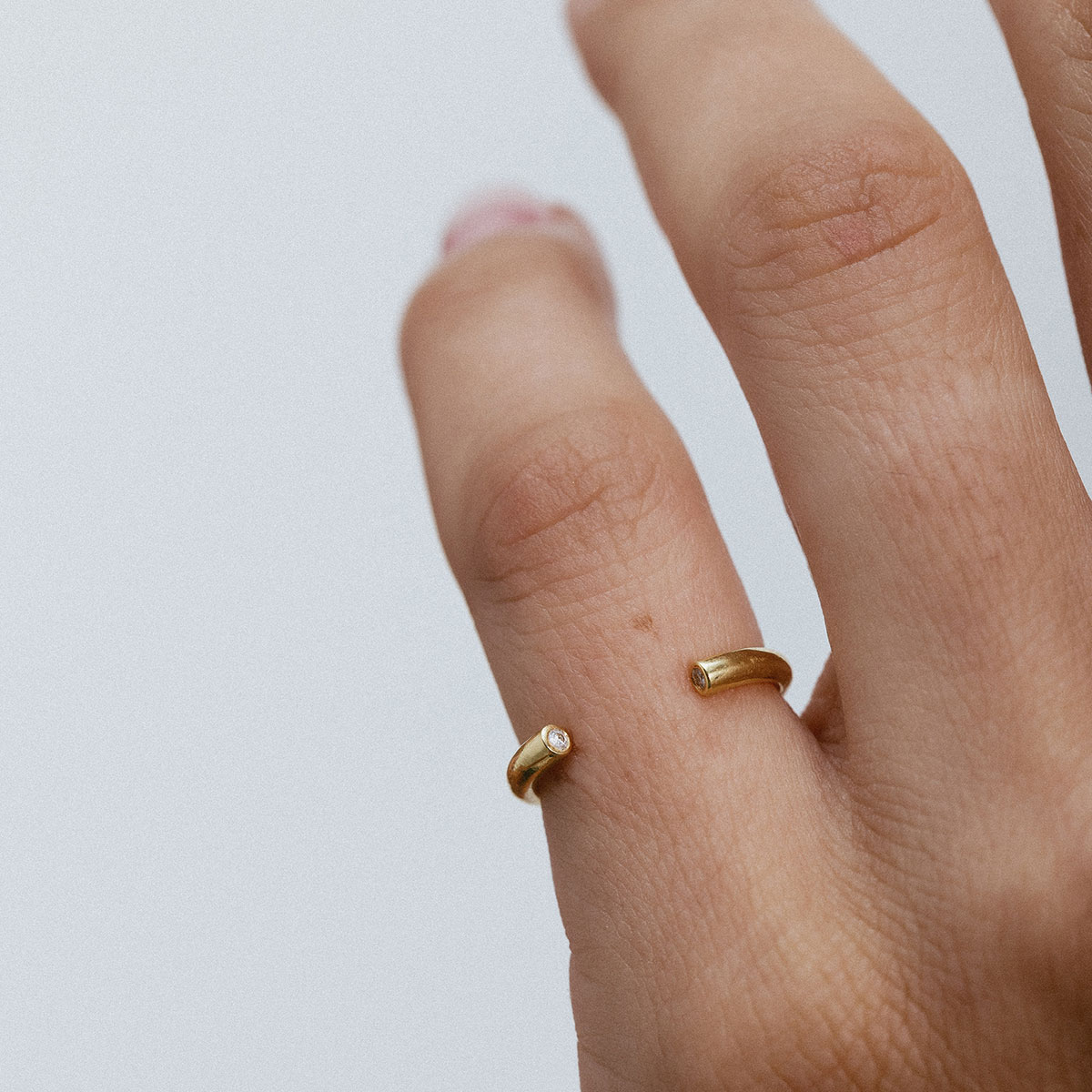 Anel minimalista aberto em ouro 18k usado no dedo mindinho de uma mão feminina.