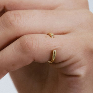 Anel minimalista aberto em ouro 18k com dois diamantes usado no dedo mindinho de uma mão feminina.
