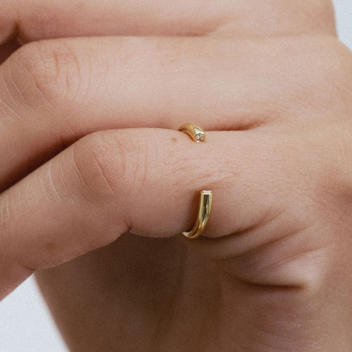 Anel minimalista aberto em ouro 18k com dois diamantes usado no dedo mindinho de uma mão feminina.