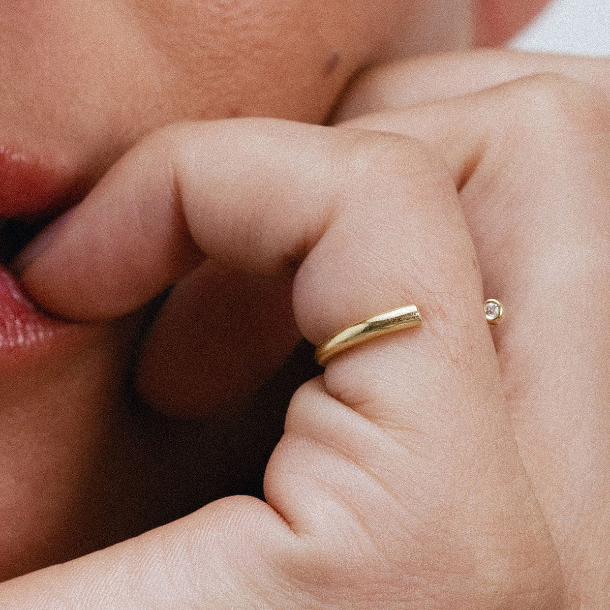 Anel minimalista aberto em ouro 18k com dois diamantes usado no dedo mindinho de uma mão feminina.