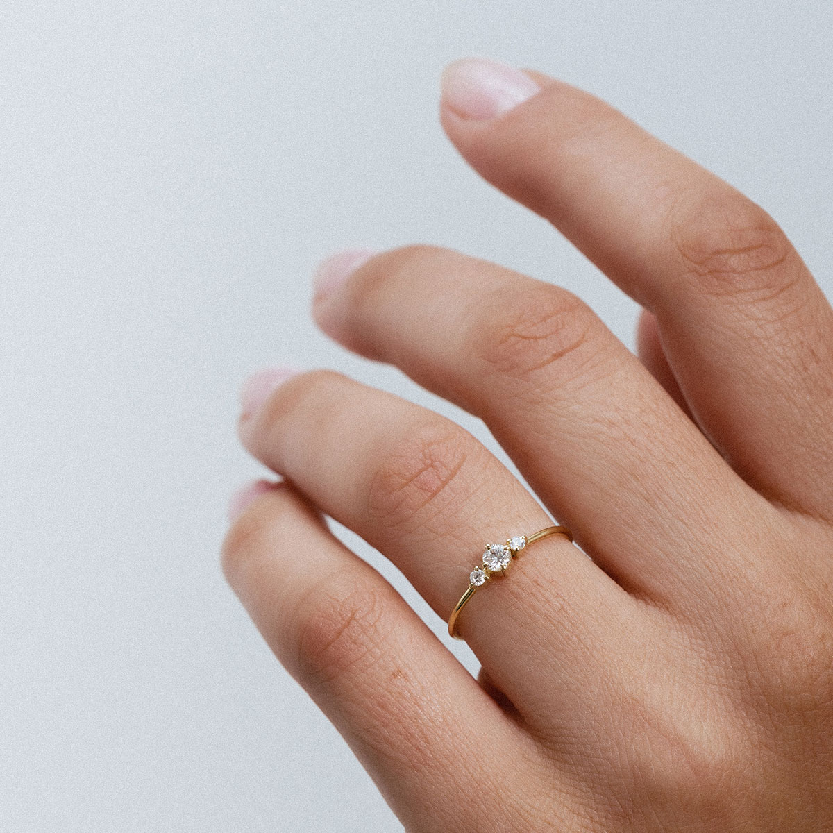 Anel em ouro 18K com três diamantes alinhados e centralizados. Anel delicado e minimalista. Aparece no dedo anelar de uma mão feminina, mais de perto mostrando sua delicadeza.