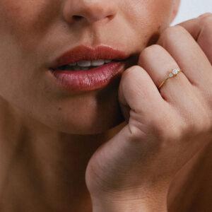Anel em ouro 18K com três diamantes alinhados e centralizados. Anel delicado e minimalista. Aparece no dedo anelar de uma mão feminina, mais de longe mostrando sua sutileza.