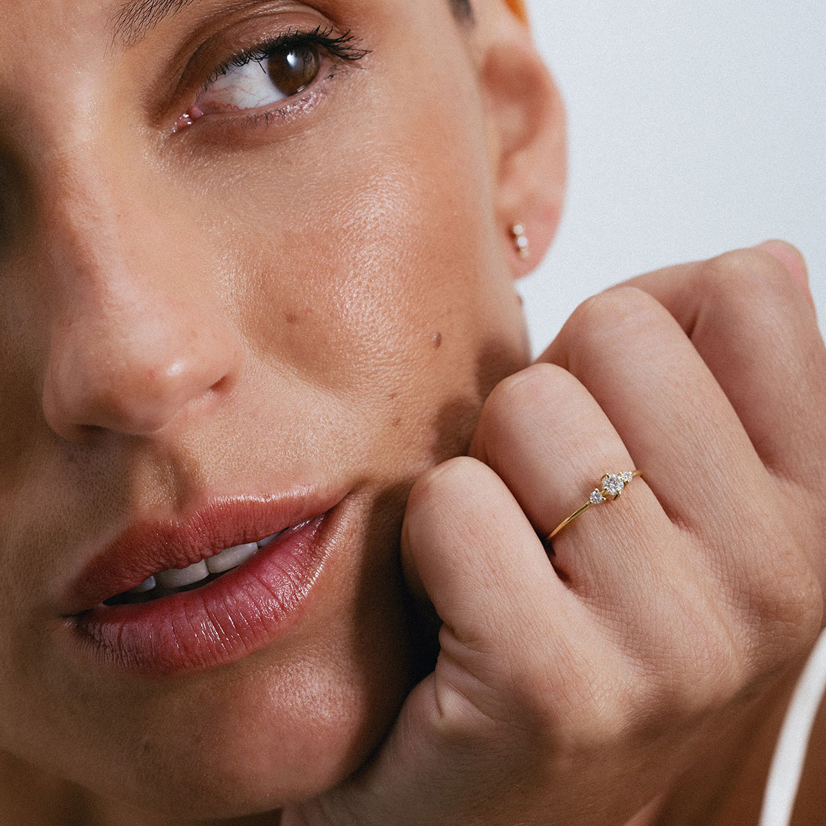 Anel em ouro 18K com três diamantes alinhados e centralizados. Anel delicado e minimalista. Aparece no dedo anelar de uma mão feminina, mais de longe mostrando sua sutileza.