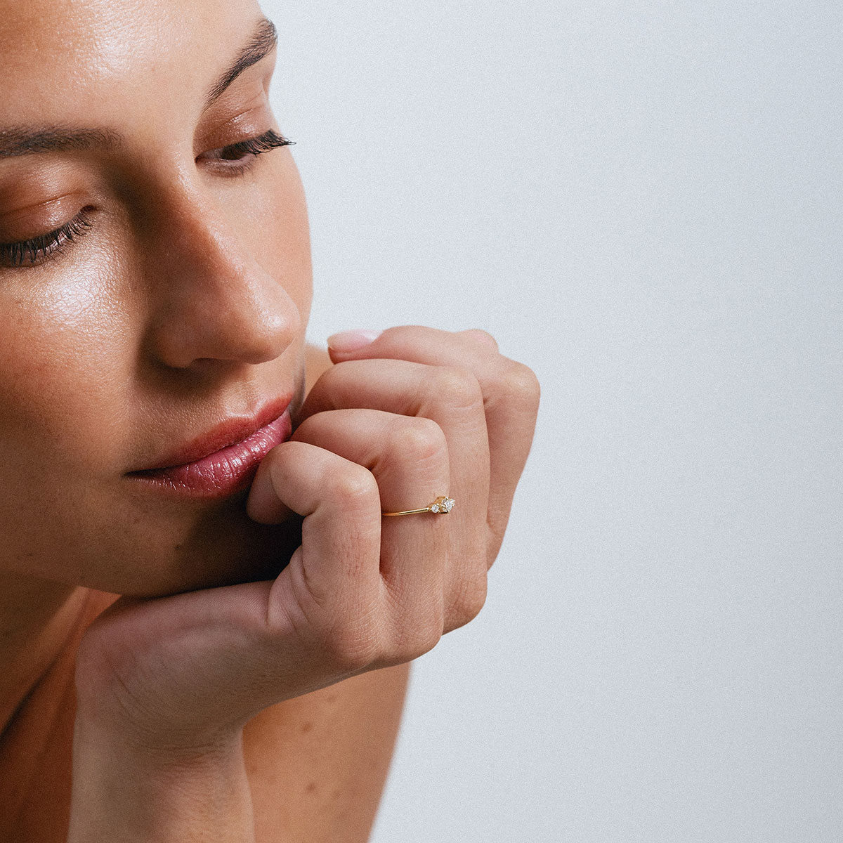 Anel em ouro 18K com três diamantes alinhados e centralizados. Anel delicado e minimalista. Aparece no dedo anelar de uma mão feminina, mais de longe mostrando sua sutileza.
