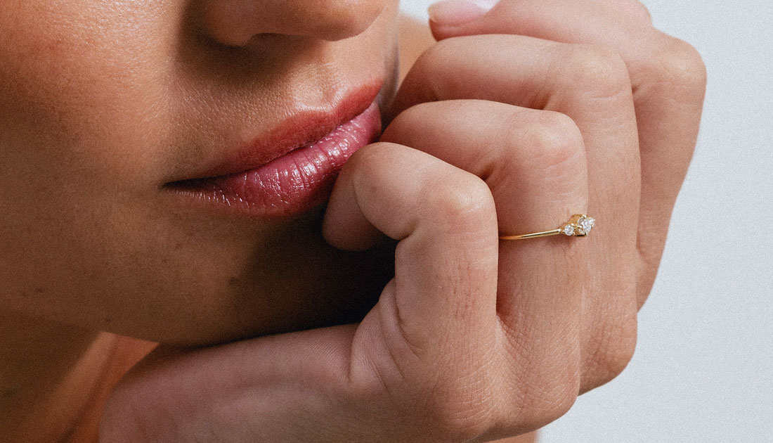 Anel em ouro 18K com três diamantes alinhados e centralizados. Anel delicado e minimalista. Aparece no dedo anelar de uma mão feminina, mais de perto, mostrando seus detalhes.