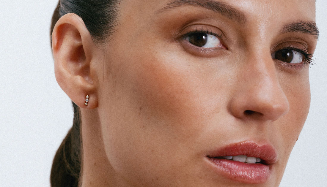 Brinco pequeno e delicado em ouro 18k com pequenos diamantes, vestido em uma mulher.