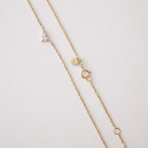 Colar em ouro 18k com diamante em lapidação gota centralizado na corrente. Colar sobre um superfície mostrando a corrente, o diamante e o fecho.