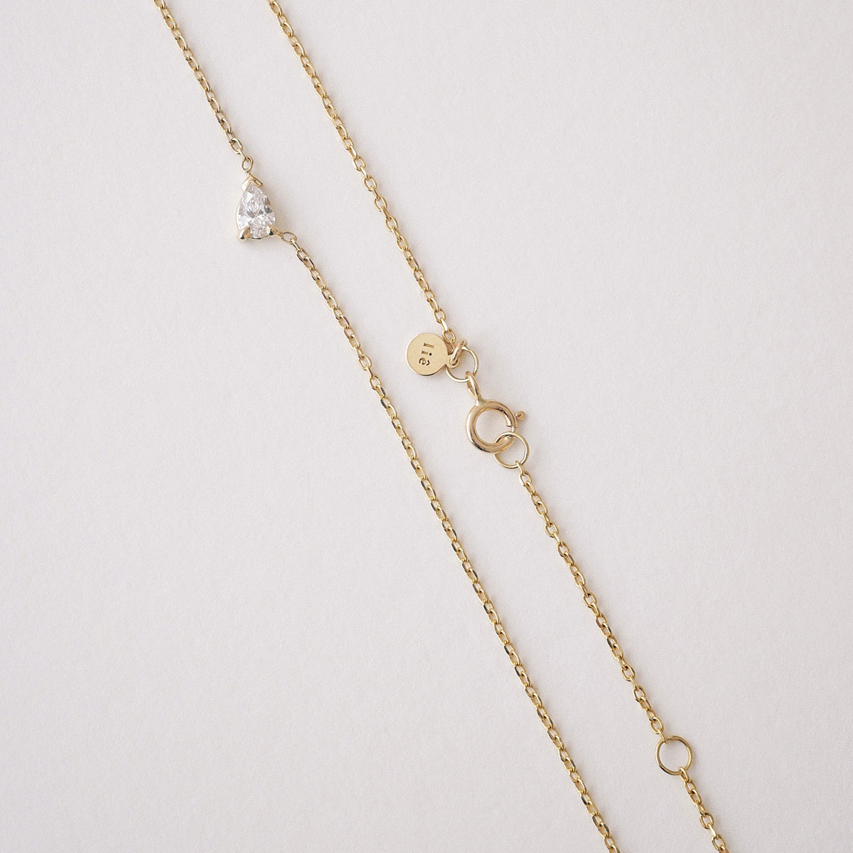 Colar em ouro 18k com diamante em lapidação gota centralizado na corrente. Colar sobre um superfície mostrando a corrente, o diamante e o fecho.