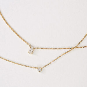 Close da composição com colar solitário de diamante oval e colar solitário de diamante de 10 pontos em ouro 18k.