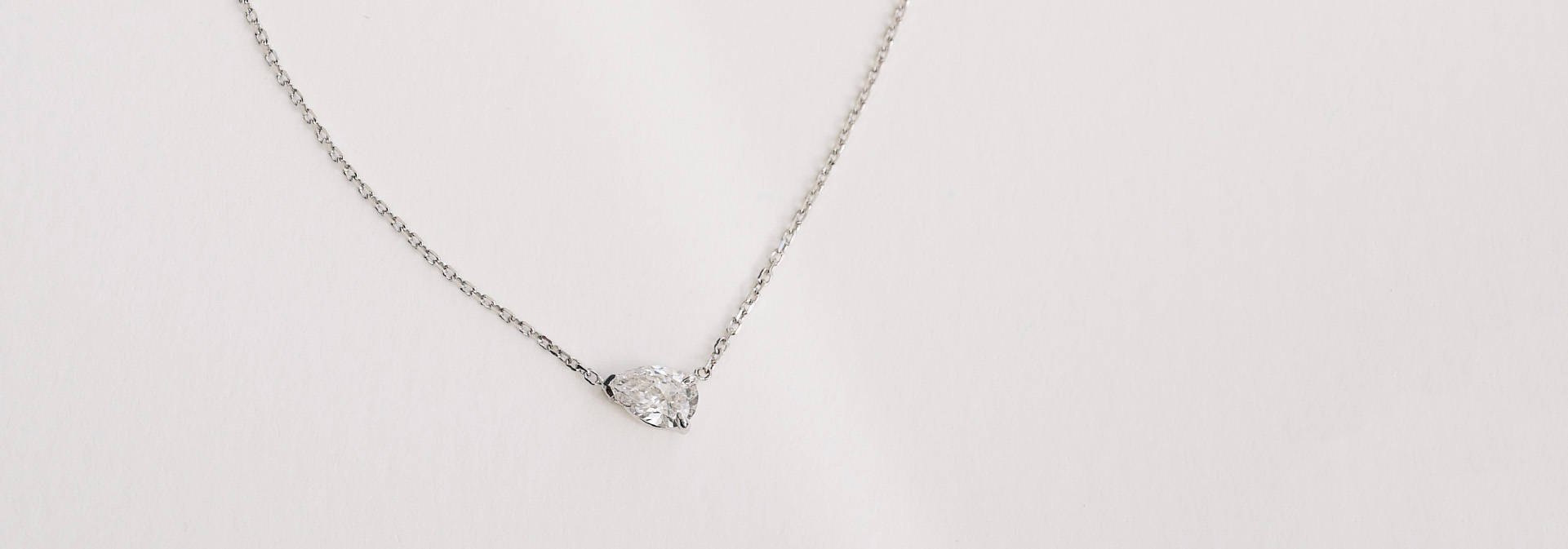 Colar delicado em ouro branco 18k com diamante em formato gota sobre fundo claro