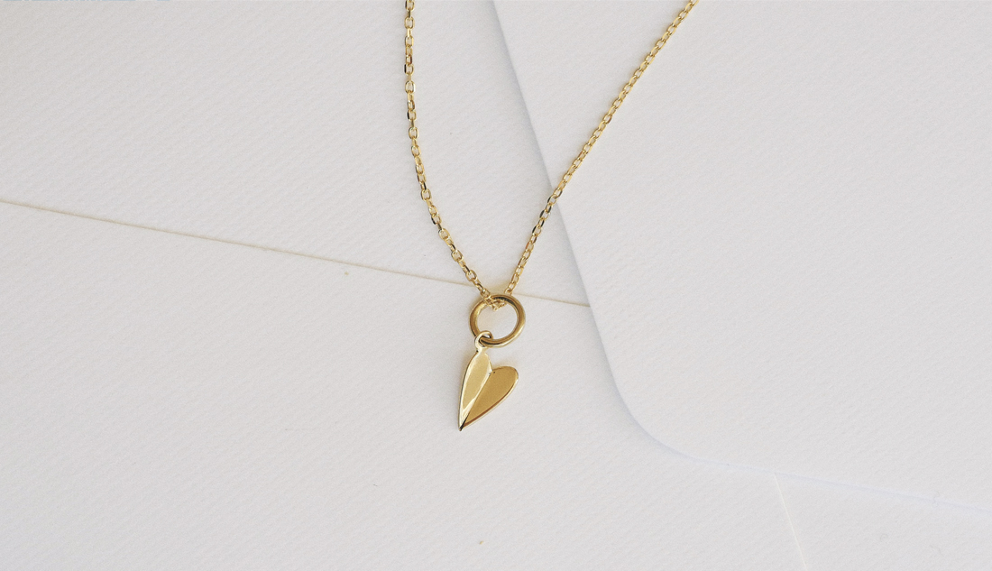 Colar com pingente Dobra Coração em ouro minimalista sobre fundo claro e elegante