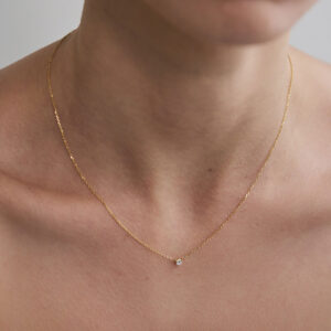 Colar solitário em ouro 18k com diamante de 10 pontos sendo usado no pescoço.