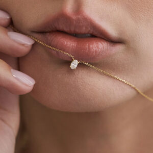Close do colar solitário com diamante oval próximo aos lábios.