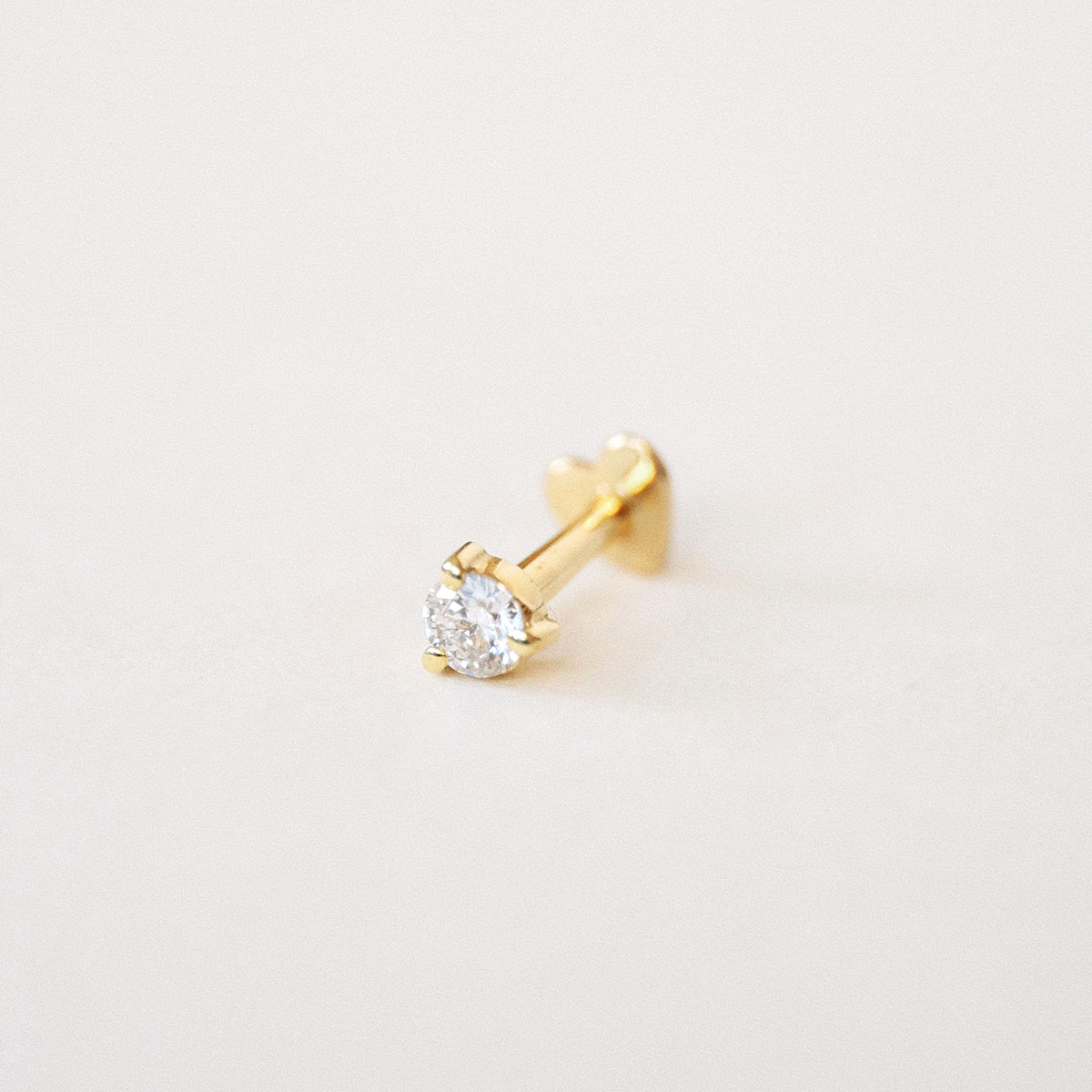 Piercing Diamante em ouro amarelo 18k com diamante redondo fotografado sobre fundo off-white.