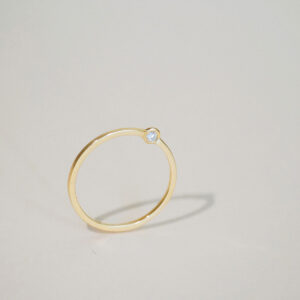 Anel Órbita em ouro 18k com diamante em design circular minimalista sobre fundo claro.