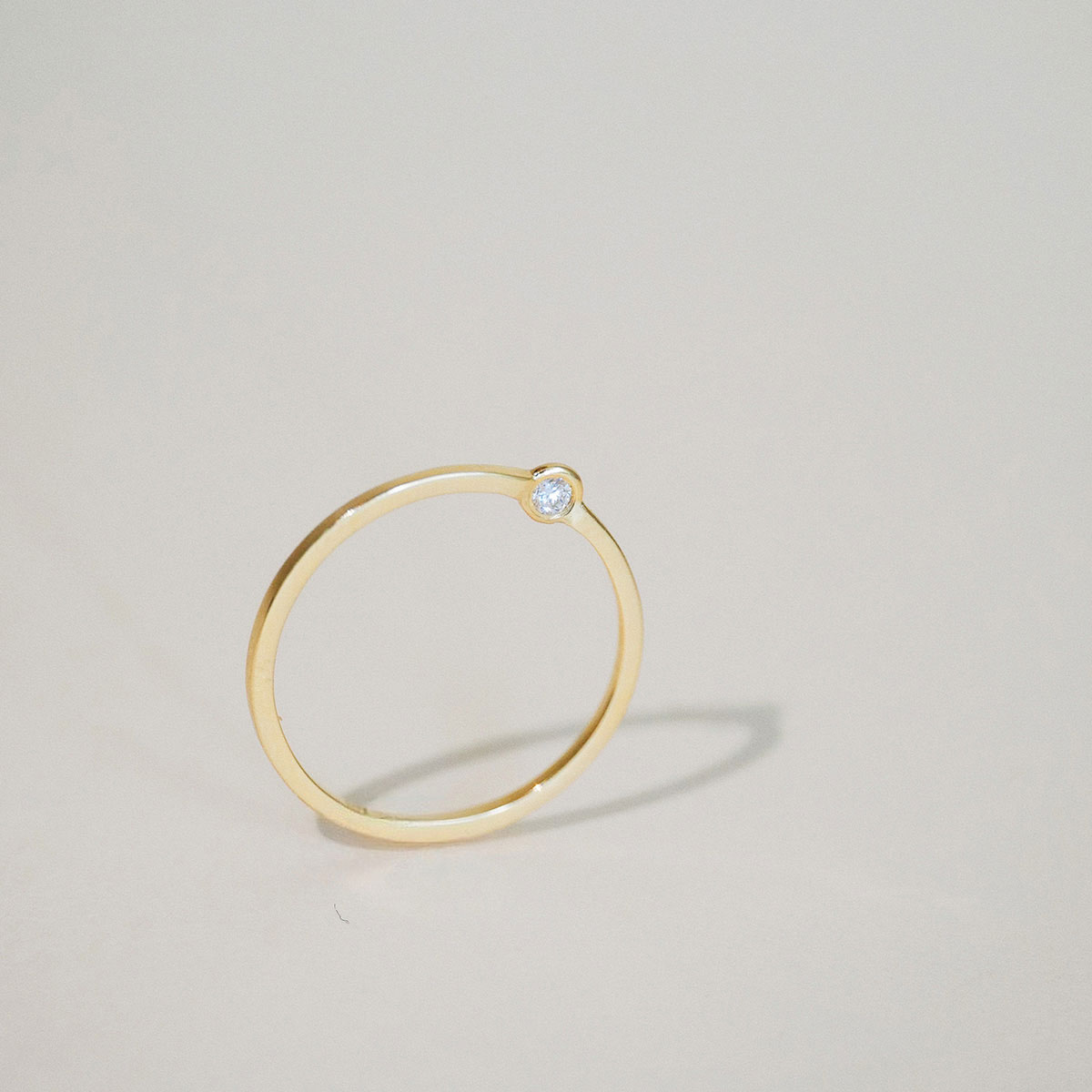 Anel Órbita em ouro 18k com diamante em design circular minimalista sobre fundo claro.