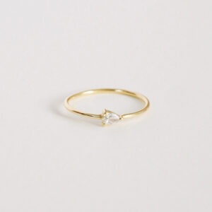 Anel solitário em ouro amarelo 18k com diamante em lapidação gota sobre fundo branco.