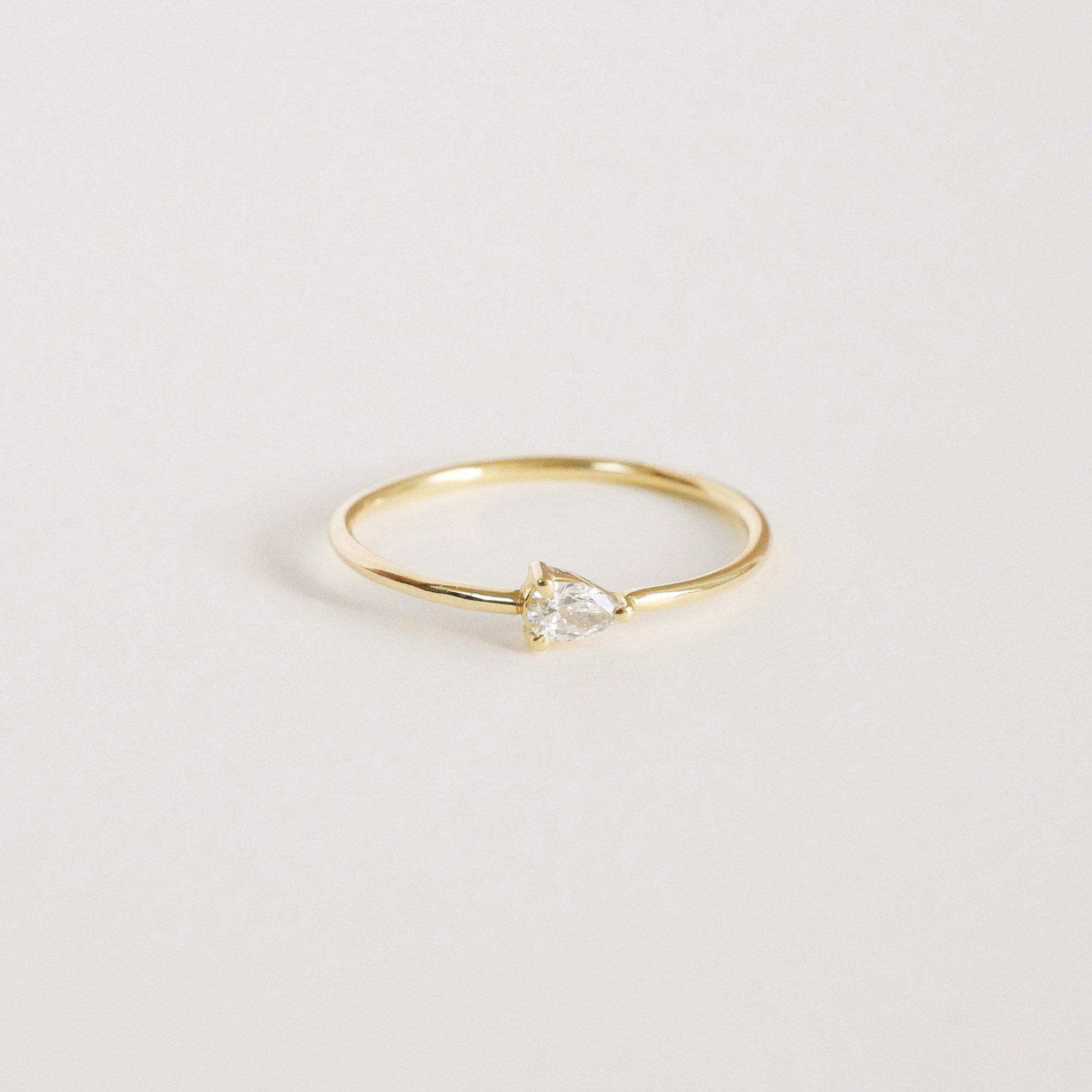Anel solitário em ouro amarelo 18k com diamante em lapidação gota sobre fundo branco.